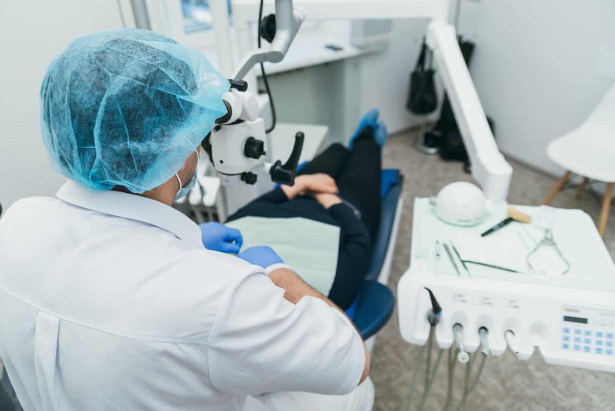 Doctor used microscope. Dentist is treating patient in modern dental office. Operation is carried out using cofferdam. Client is inserted and restored teeth, make denture.